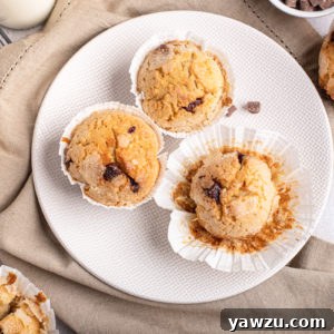 Three Chocolate Chip Muffins on white plate, surrounded by additional muffins, showcasing their golden tops and tender texture.