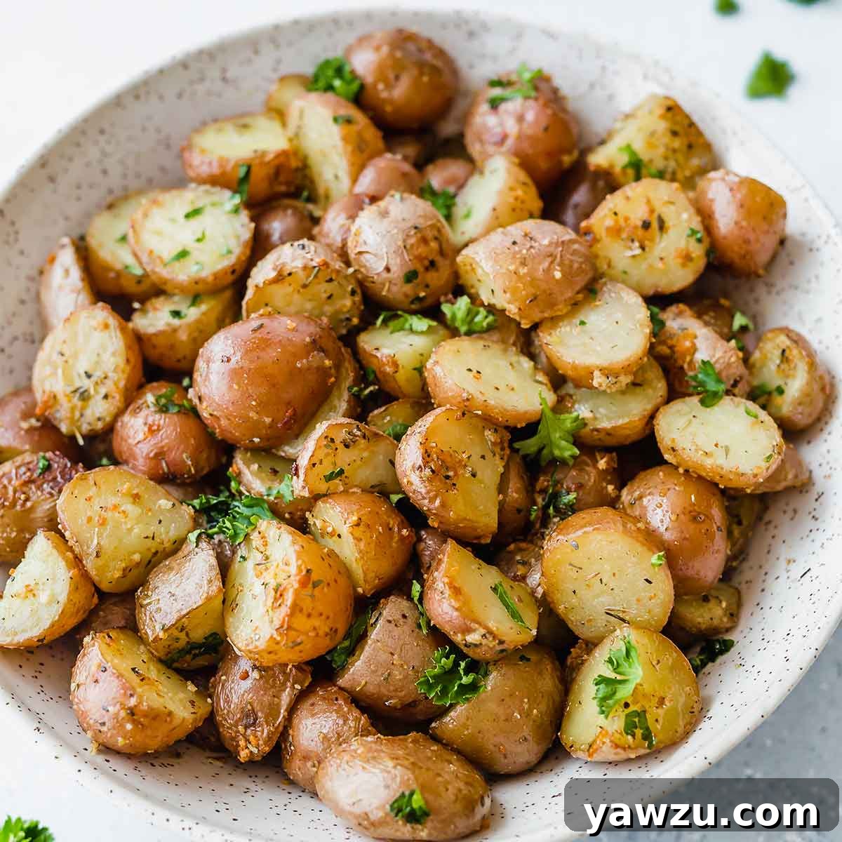 A rustic pottery bowl filled with perfectly roasted red potatoes, golden brown and garnished with fresh herbs.