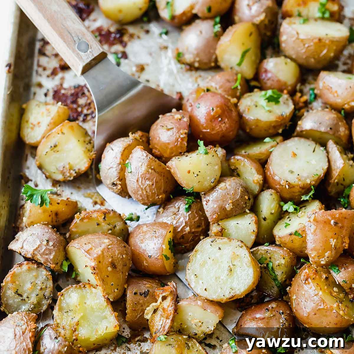A silver spatula lifting perfectly roasted red potatoes from a baking sheet, showcasing their golden-brown and crispy texture.