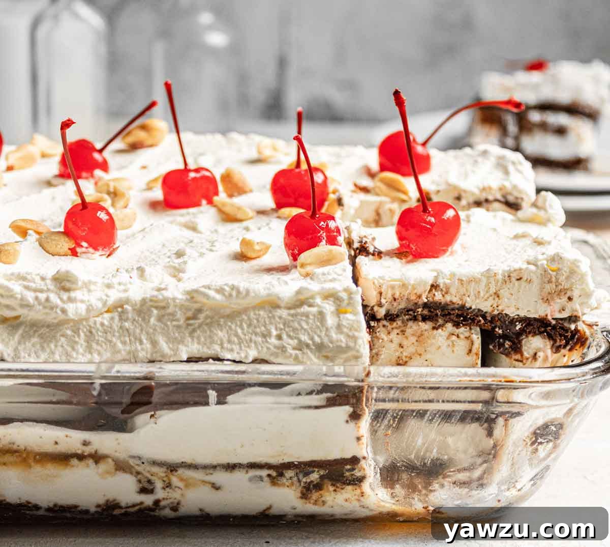 A close-up, side view of a perfectly assembled ice cream sandwich cake in a glass baking dish, showcasing the distinct layers of ice cream sandwiches, dark fudge, and white whipped topping, ready to be sliced.