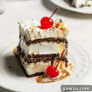 A close-up of a square slice of easy ice cream sandwich cake, topped with whipped cream, chocolate syrup, chopped nuts, and a cherry, served on a white plate.