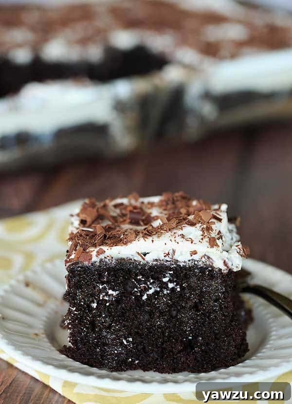 A generous serving of Chocolate Mudslide Poke Cake, garnished with delicate shaved chocolate. The rich, dark chocolate cake base is visible beneath the creamy topping, promising a boozy, sweet, and satisfying dessert experience. | browneyedbaker.com