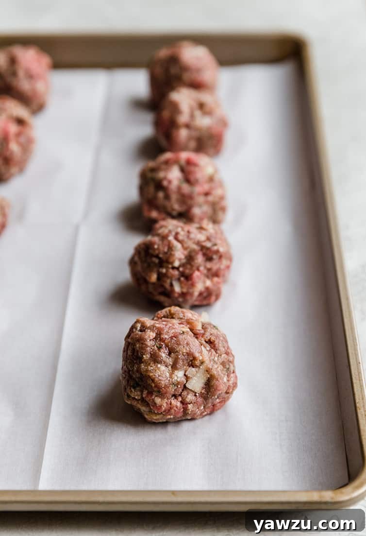 Neatly shaped meatballs arranged on a parchment-lined baking sheet, ready for baking.