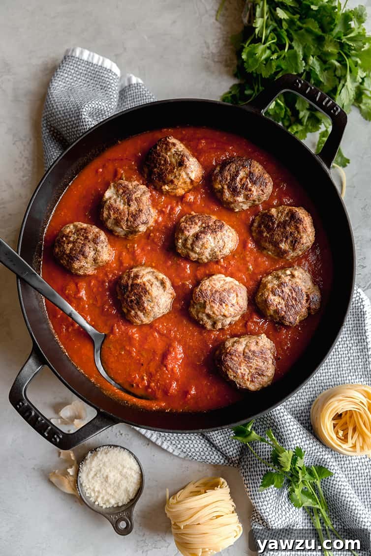 Golden-brown meatballs being gently added to a simmering pot of rich red marinara sauce.