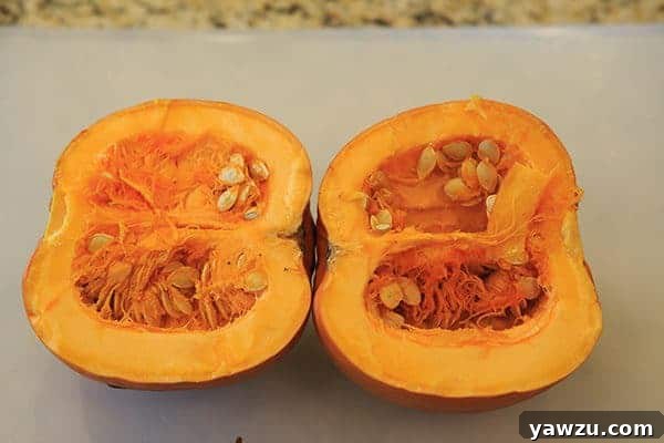 A sharp chef's knife slicing a sugar pumpkin in half on a wooden cutting board.