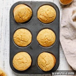 A close up of a non-stick muffin tin with cornbread muffins on a white counter with a light beige towel to the right.