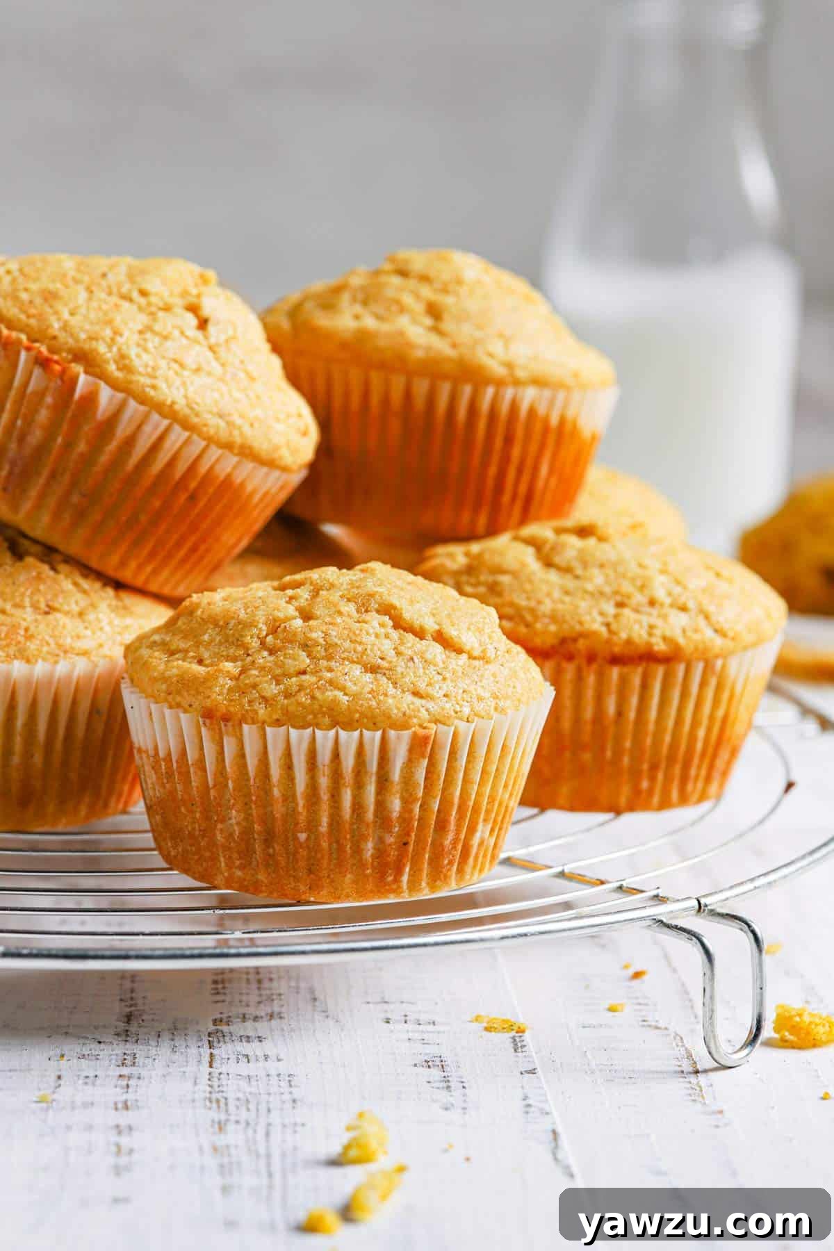 A close up of a pile of cornbread muffins on a wire rack with a jug of milk in the back right.