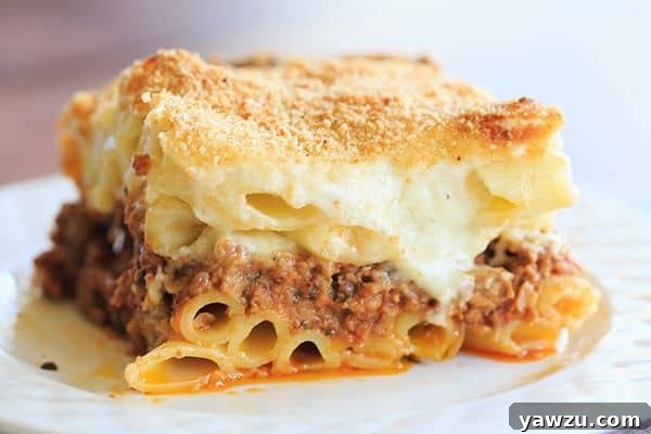A beautifully presented classic pastitsio, showcasing layers of golden-brown béchamel, ziti pasta, and a rich beef and lamb meat sauce, ready to be served.