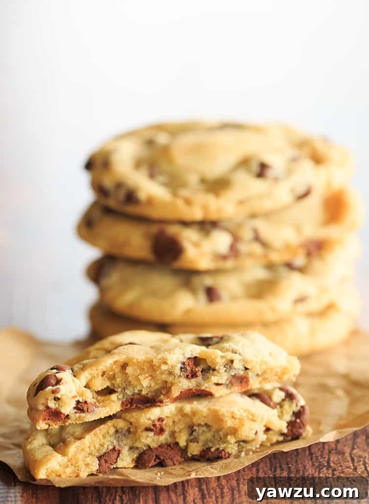 One perfectly baked chocolate chip cookie, warm and inviting, split in half to reveal its soft, gooey interior, placed in front of a tempting stack of other homemade cookies.