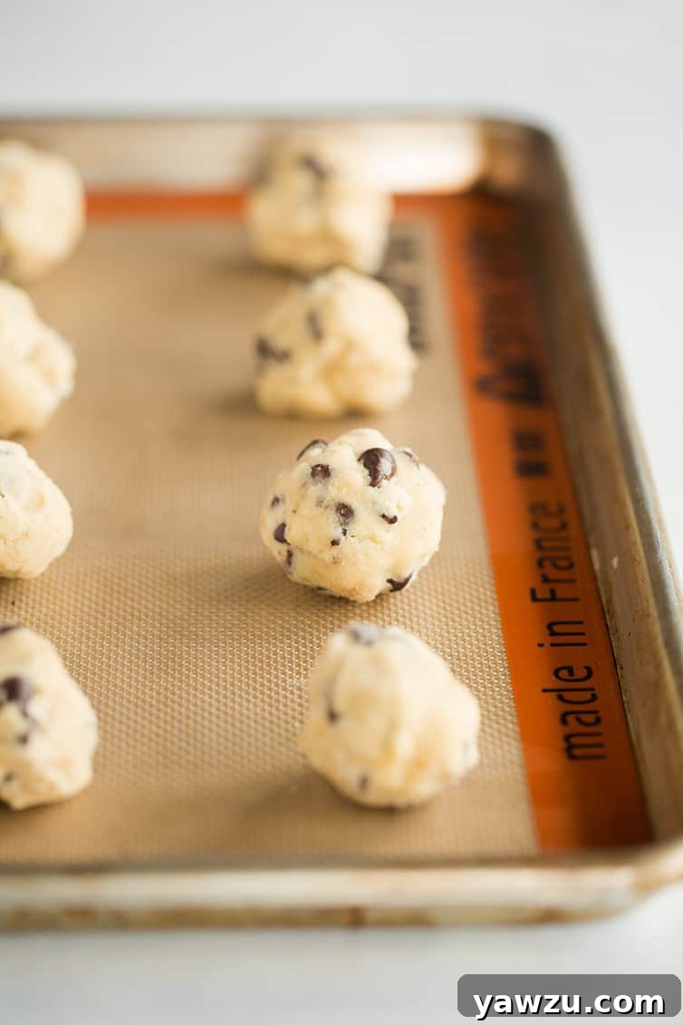 Neatly portioned balls of raw chocolate chip cookie dough arranged on a baking sheet, ready for chilling and then baking.