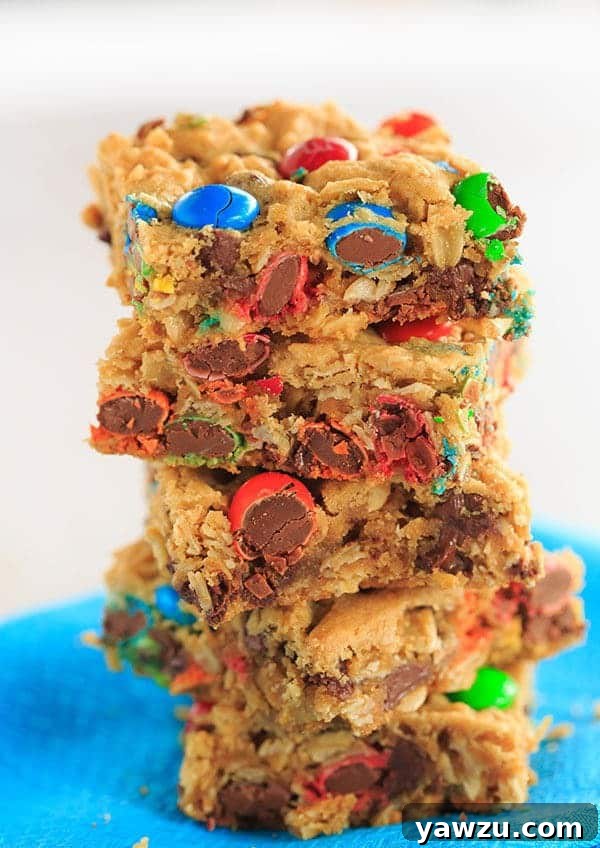 A generous slice of Monster Cookie Bar, showcasing its thick, chewy texture and abundance of colorful M&M's and chocolate pieces.