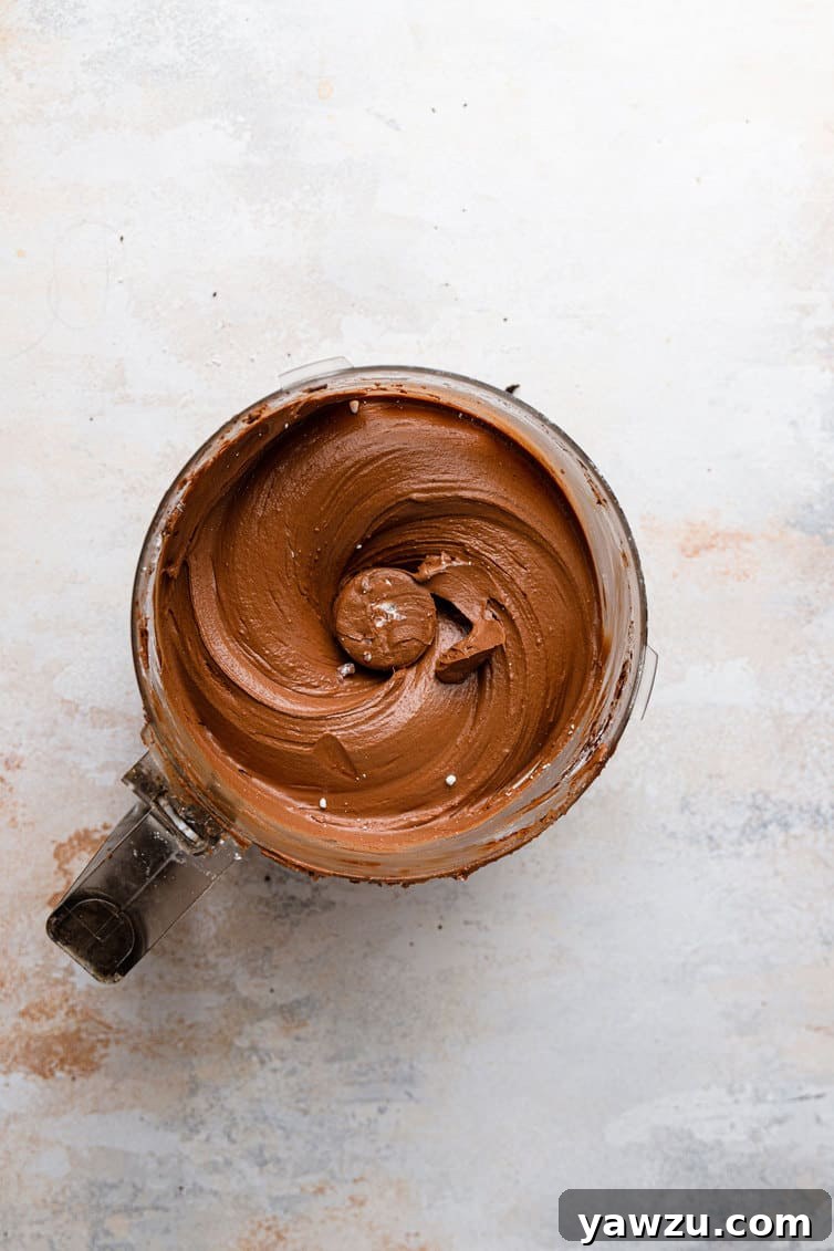 Lush, dark chocolate fudge frosting, perfectly smooth and glistening, filling the bowl of a food processor.