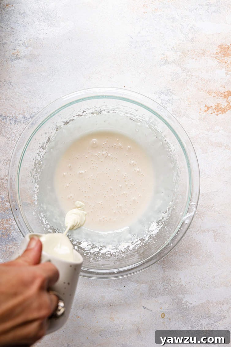 Molten white chocolate being carefully poured from a small bowl into a larger mixing bowl.