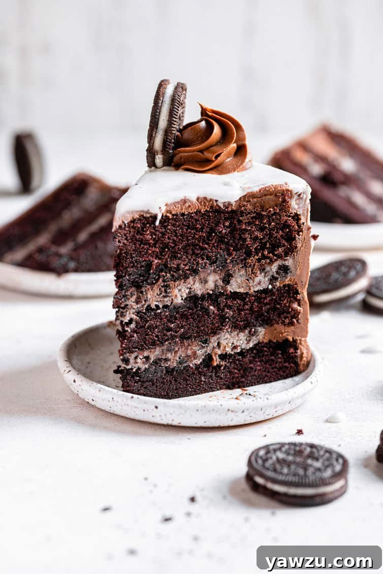 A perfect slice of Oreo cake, showcasing its distinct layers, elegantly presented on a white plate with whole Oreo cookies scattered around it.