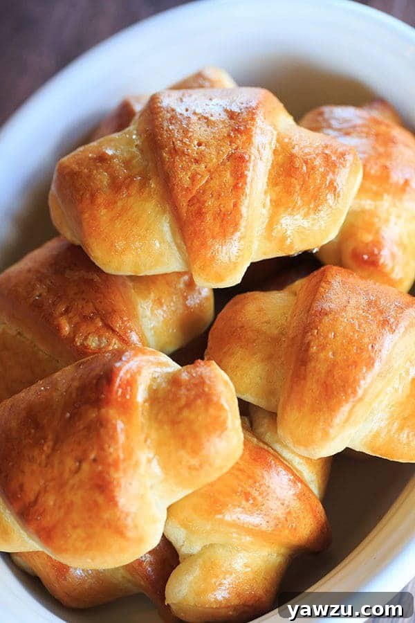 Perfectly baked golden-brown crescent rolls, showcasing their signature curved shape and a soft, inviting texture, resting on a serving dish.