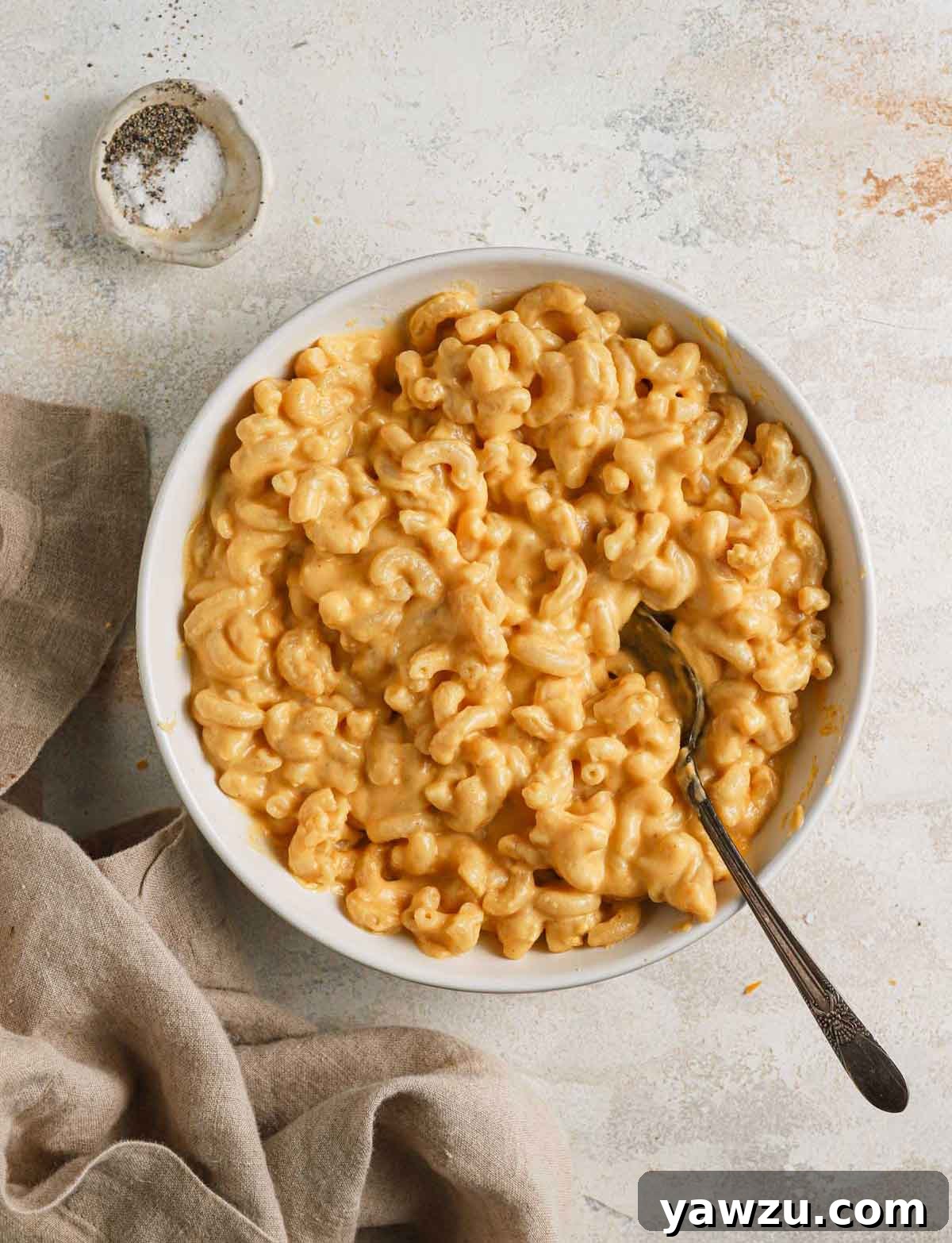 Overhead photo of a white bowl filled with creamy stovetop mac and cheese, garnished with a sprinkle of fresh black pepper.