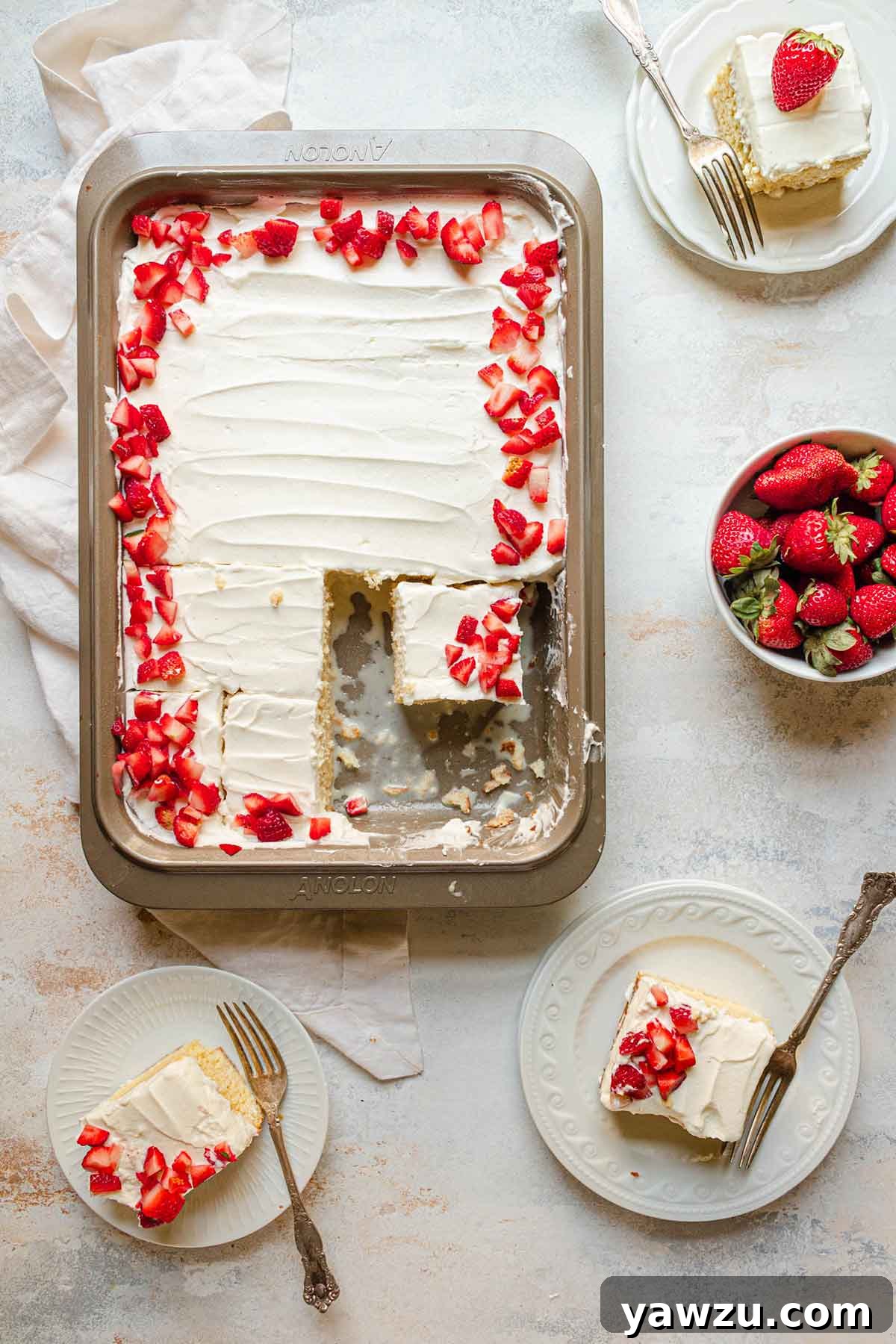 Overhead photo of pan of tres leches cake topped with strawberries and plates with single slices on them.