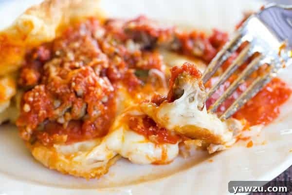 A large deep dish biscuit pizza, cut into generous squares, revealing the layers of cheese, meat, and sauce on a golden-brown biscuit crust.