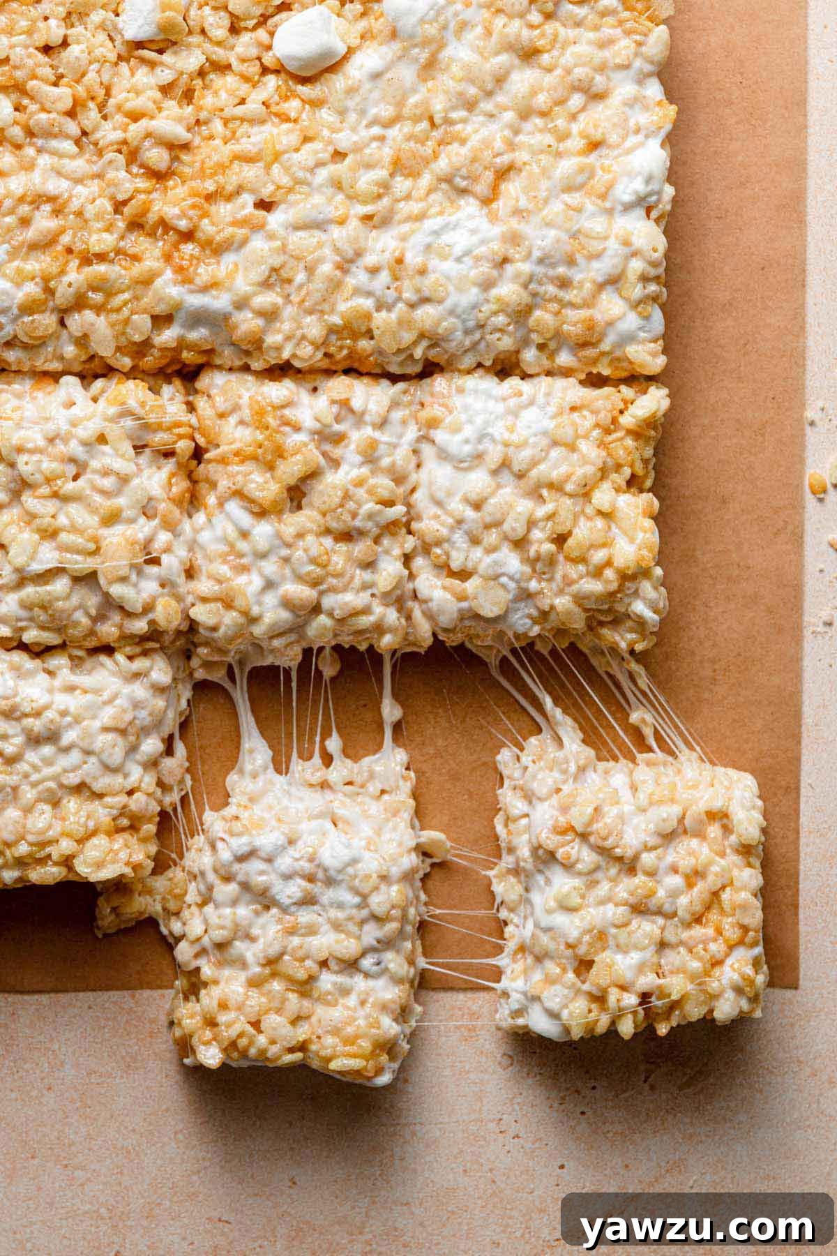 Overhead photo of homemade rice krispie treats on a cutting board, with two being pulled away, showcasing their gooey texture.