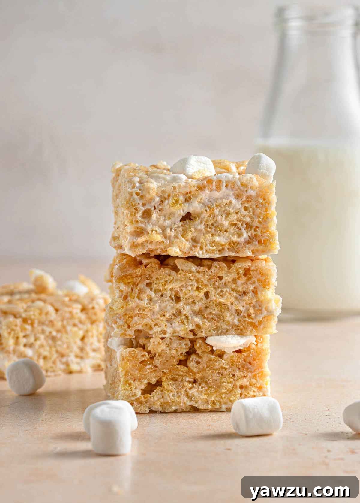 Three perfectly stacked rice krispie treats with a vintage milk jar in the soft-focus background, highlighting their thick, substantial appearance.