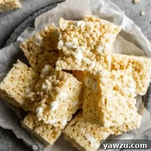 A square photo from the top down of a stack of rice krispie treats on a parchment paper on a grey plate.