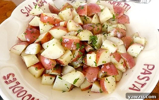 Close-up of a serving bowl filled with herbed balsamic potato salad, showcasing quartered red potatoes and fresh green herbs.