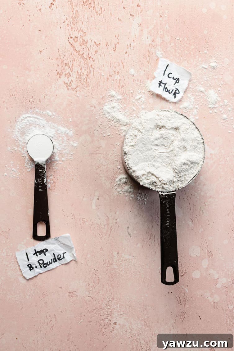 A measuring spoon of baking powder next to a measuring cup of flour.
