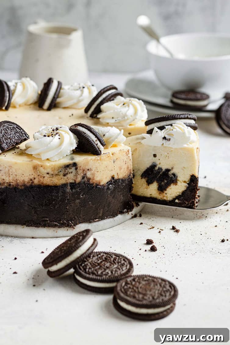 A perfectly sliced Oreo cheesecake with a generous piece removed, surrounded by whole and crushed Oreo cookies on a rustic wooden counter.