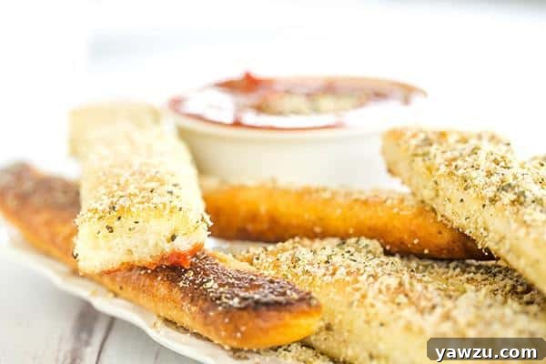 A selection of crispy, buttery garlic breadsticks and a bowl of savory red dipping sauce, ready to be enjoyed.