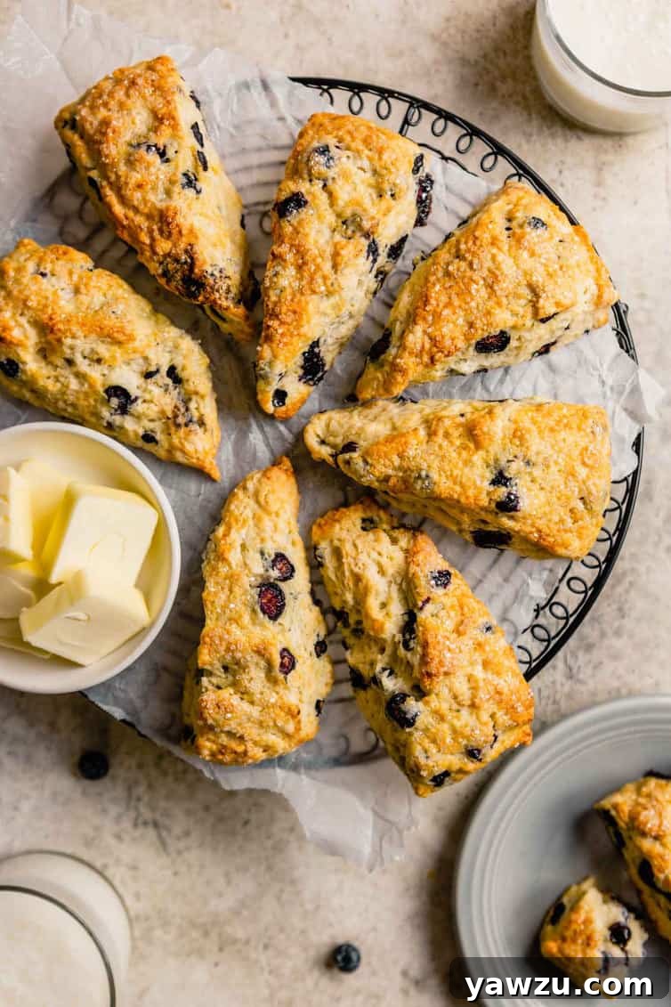 A black wire cooling rack covered in parchment paper with golden-brown buttermilk scones on top, with a small bowl of butter positioned to the left of the cooling rack, ready to be served.