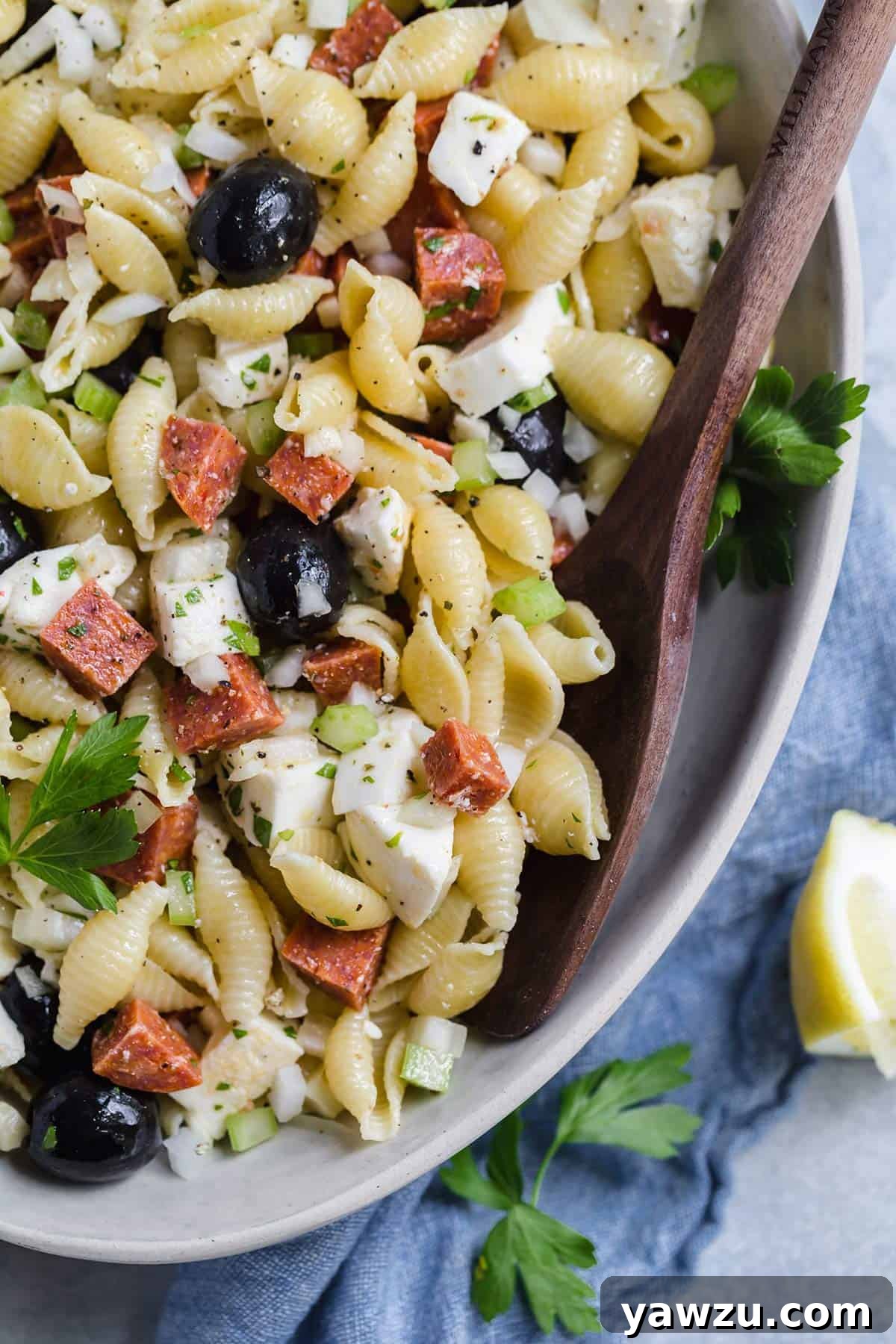 Close-up photo of a bowl filled with colorful Italian pasta salad, featuring a wooden spoon resting in it, highlighting the vibrant ingredients and inviting texture.