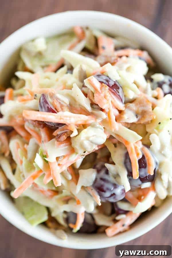 A vibrant, loaded coleslaw featuring a colorful mix of cabbage, crisp bacon, crumbled cheese, juicy red grapes, and crunchy sunflower seeds, perfect for a summer picnic or BBQ.