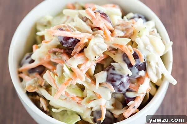 Close-up of the loaded coleslaw showing the texture and mix of ingredients like shredded cabbage, cheddar cheese, bacon bits, and halved red grapes.