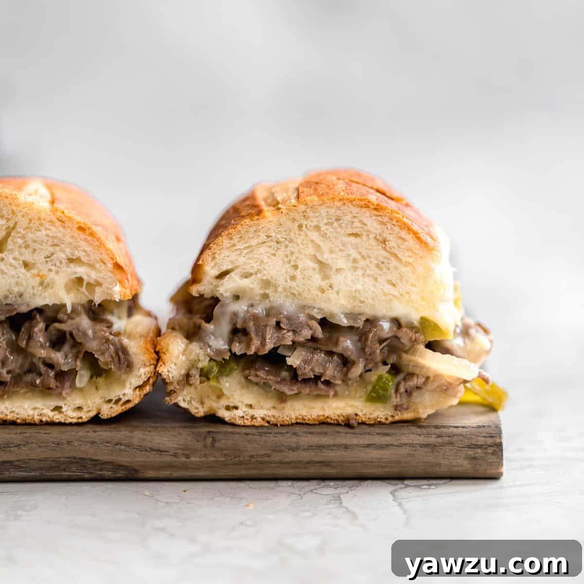 A perfectly assembled Homemade Philly Cheesesteak, showing the rich, cheesy steak, onions, and peppers overflowing from a golden hoagie roll.