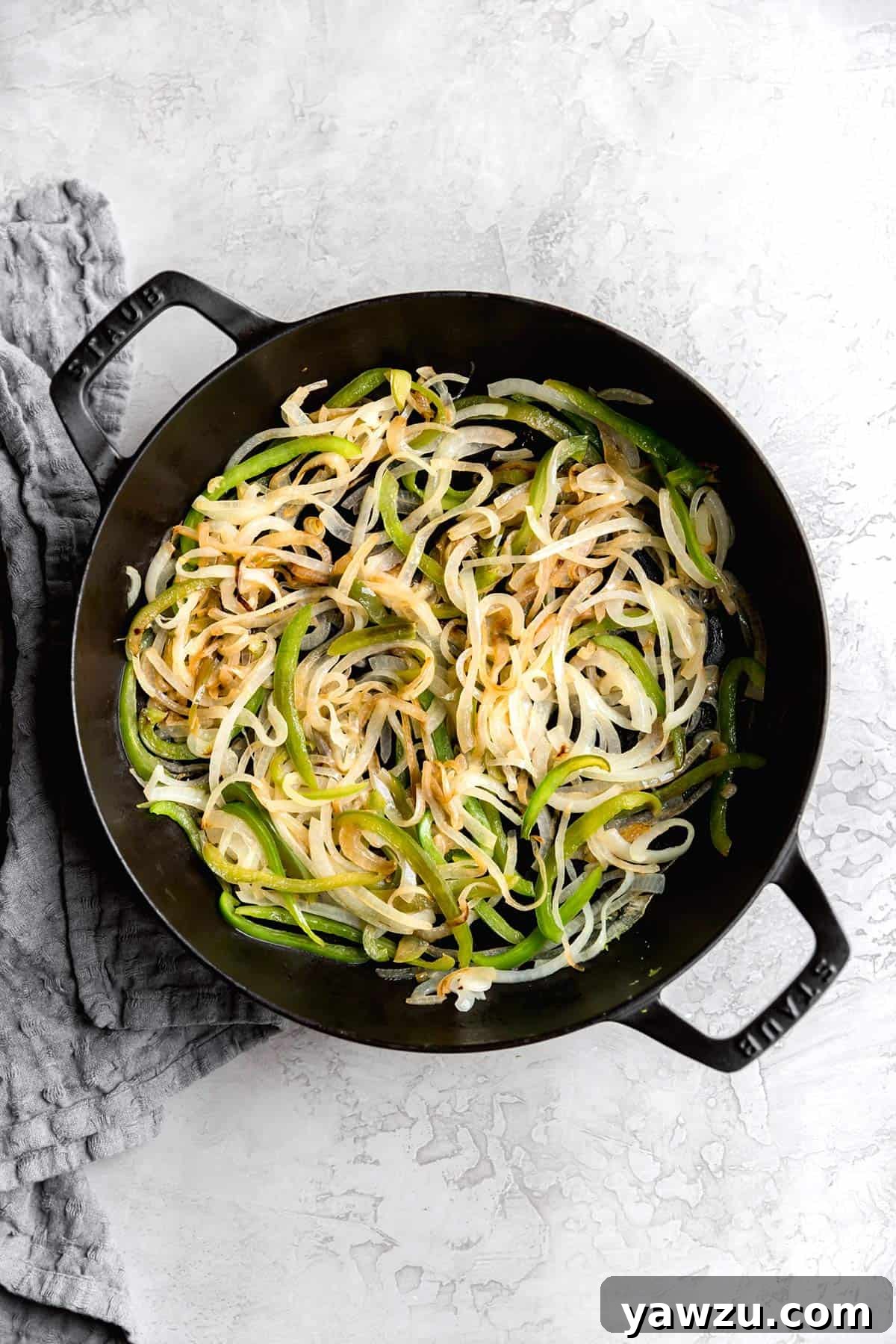 Sautéed onions and bell peppers browning in a skillet, creating a flavorful base for the Philly cheesesteak.