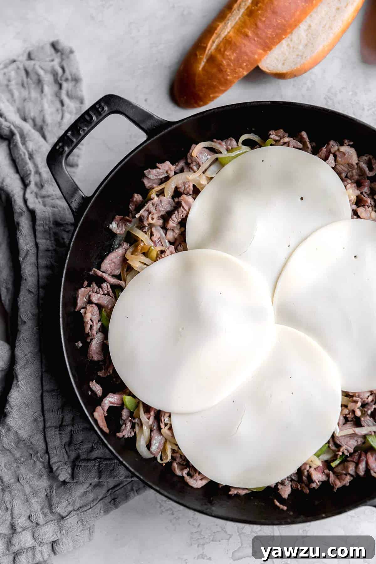 Melted provolone cheese being stirred into the cooked steak, onions, and peppers mixture in a skillet, creating a rich, gooey filling.