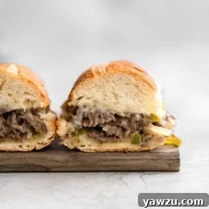 Two philly cheesesteak sandwiches on a wooden cutting board with the insides exposed showing the cheesy meat filling.