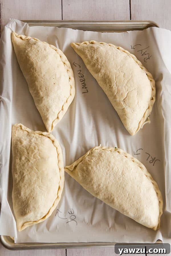 Labeled calzones on a baking sheet, ready for baking, showcasing personalization