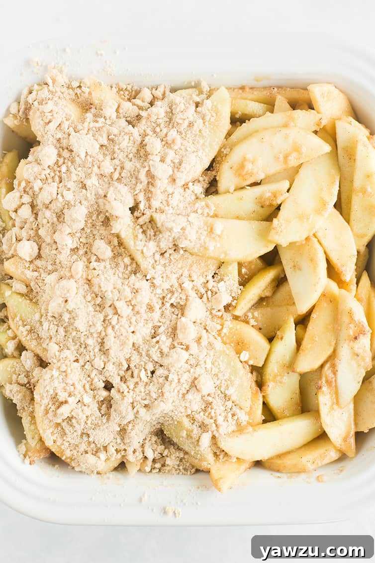 Apple crisp filling in a pan with topping over half of it.