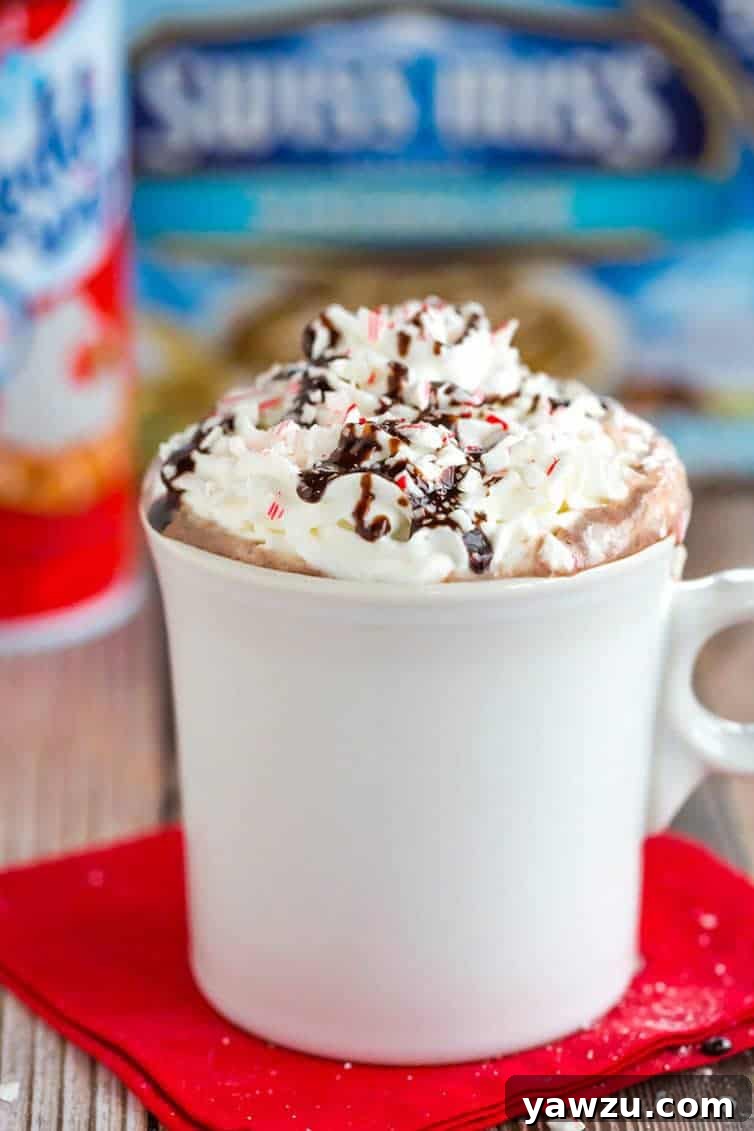 A vibrant, overhead shot showcasing two mugs of Peppermint Bark Hot Chocolate, each exquisitely topped with whipped cream, chocolate syrup drizzles, and colorful crushed candy cane sprinkles, ready for a festive celebration.