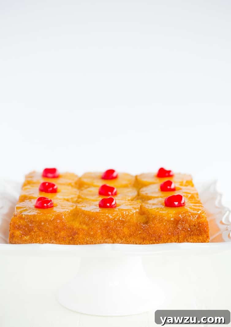 A perfectly baked homemade pineapple upside down cake on a square white cake dish, showcasing the golden caramelized pineapple and cherry topping.