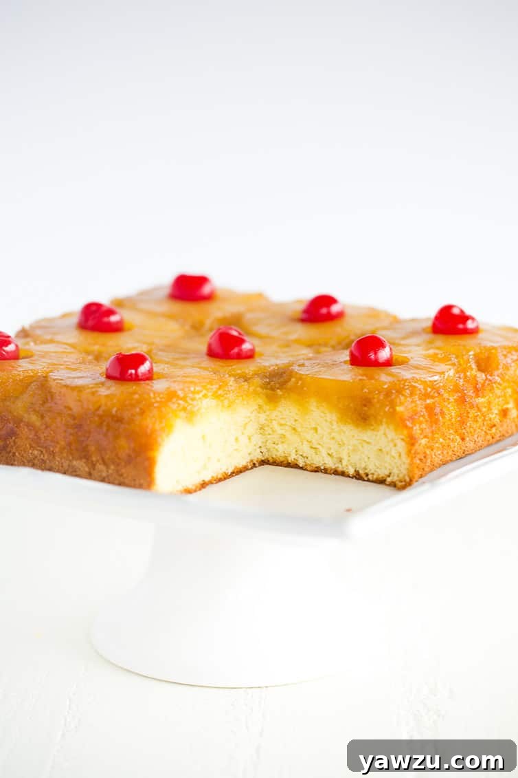 A slice of pineapple upside down cake removed from the main cake on a white platter, revealing the moist interior and fruity topping.