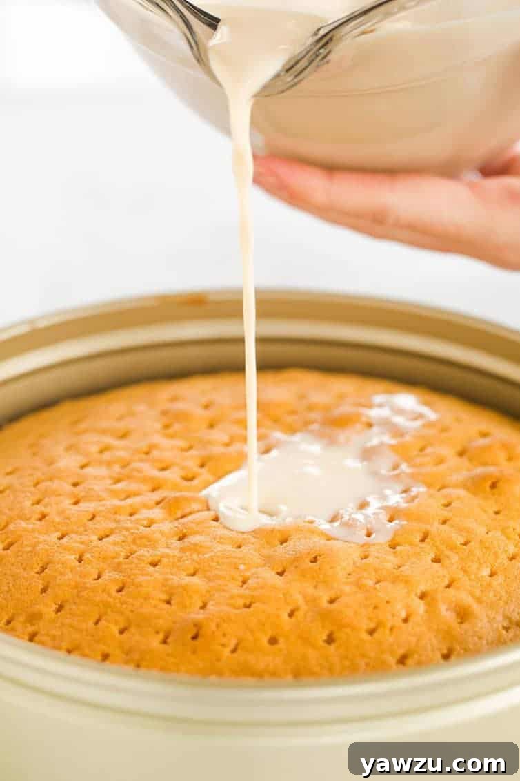 Pouring the three-milk mixture all over the caramel tres leches cake, showing the impressive height of the cake.