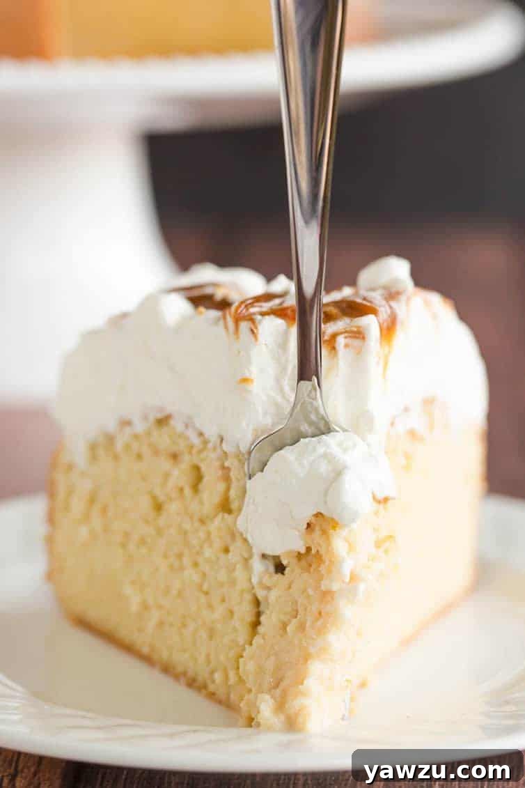 Take a big forkful of a slice of caramel tres leches cake, showing the layers of cake, soak, and whipped cream.