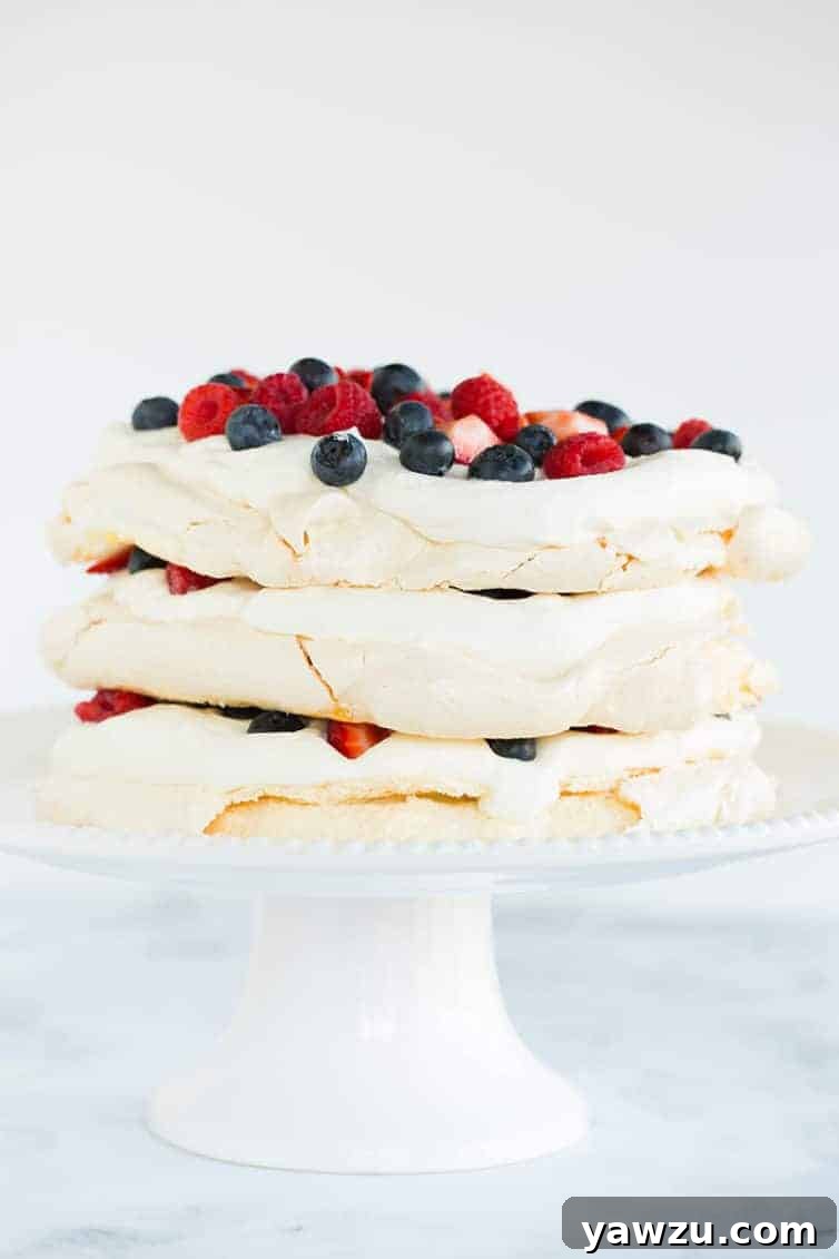 Three layers of pavlova filled and topped with whipped cream and berries, ready to be served.