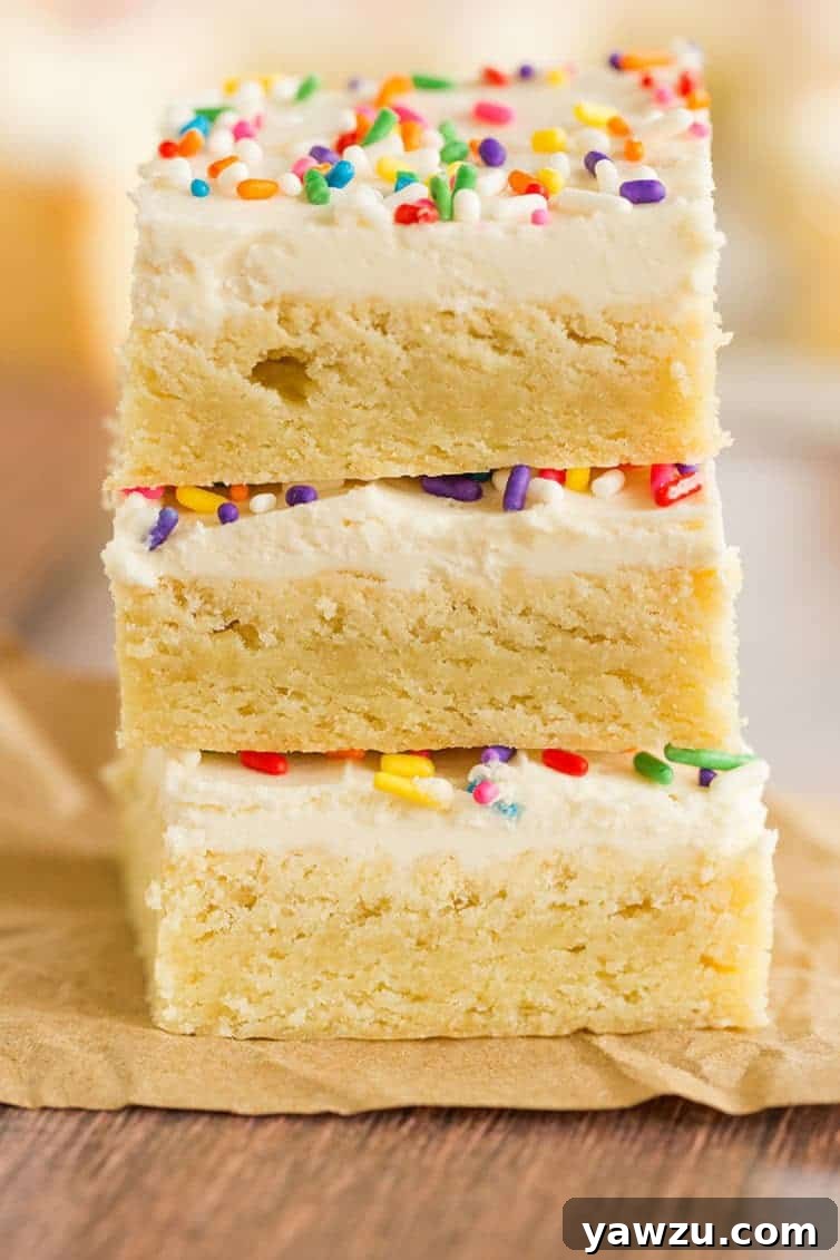 A stack of three delightfully frosted sugar cookie bars adorned with colorful sprinkles, showcasing their soft texture.