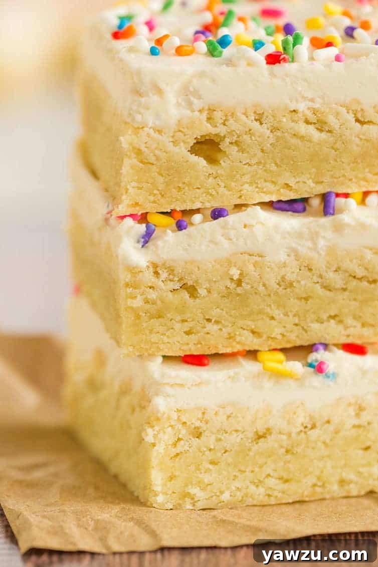 A delightful close-up shot of a stack of three frosted sugar cookie bars, highlighting the smooth vanilla buttercream and delicate sprinkles.