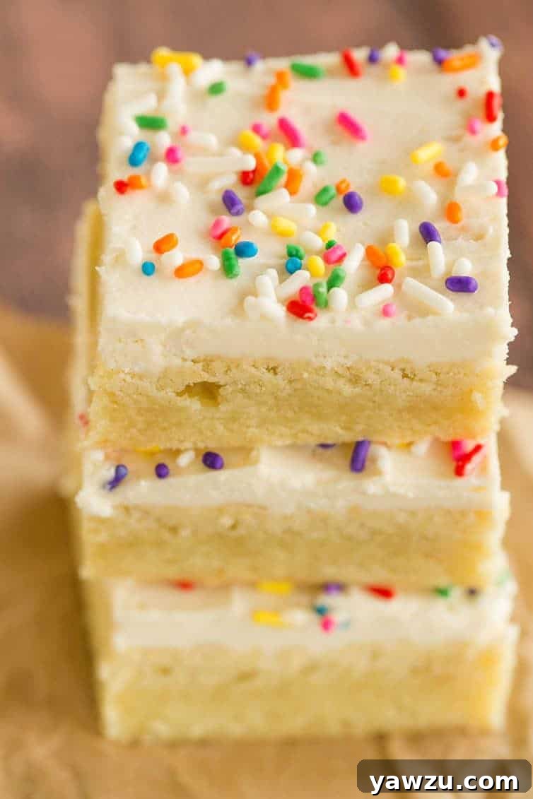 An inviting overhead shot of a stack of three frosted sugar cookie bars, complete with colorful sprinkles, set against a clean background.