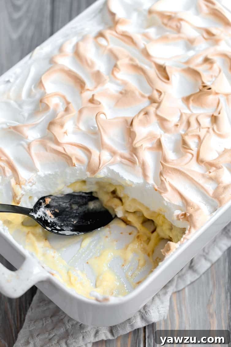 A pan of traditional Southern banana pudding with a corner scooped out, showing layers of wafers, bananas, and pudding, topped with golden meringue.