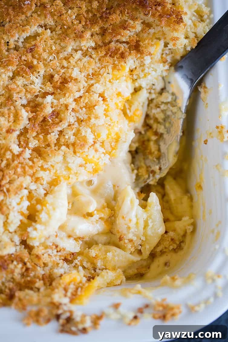 A large scoop being taken from a bubbling bowl of Chrissy Teigen's Mac and Cheese, showing its creamy texture.